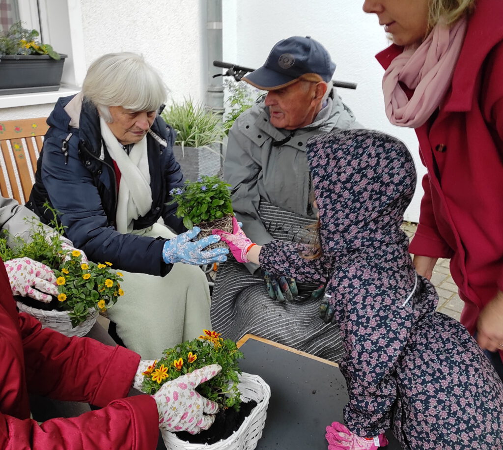 Senioren der Tagespflege pflanzen gemeinsam mit Kita Kindern Blumen ein